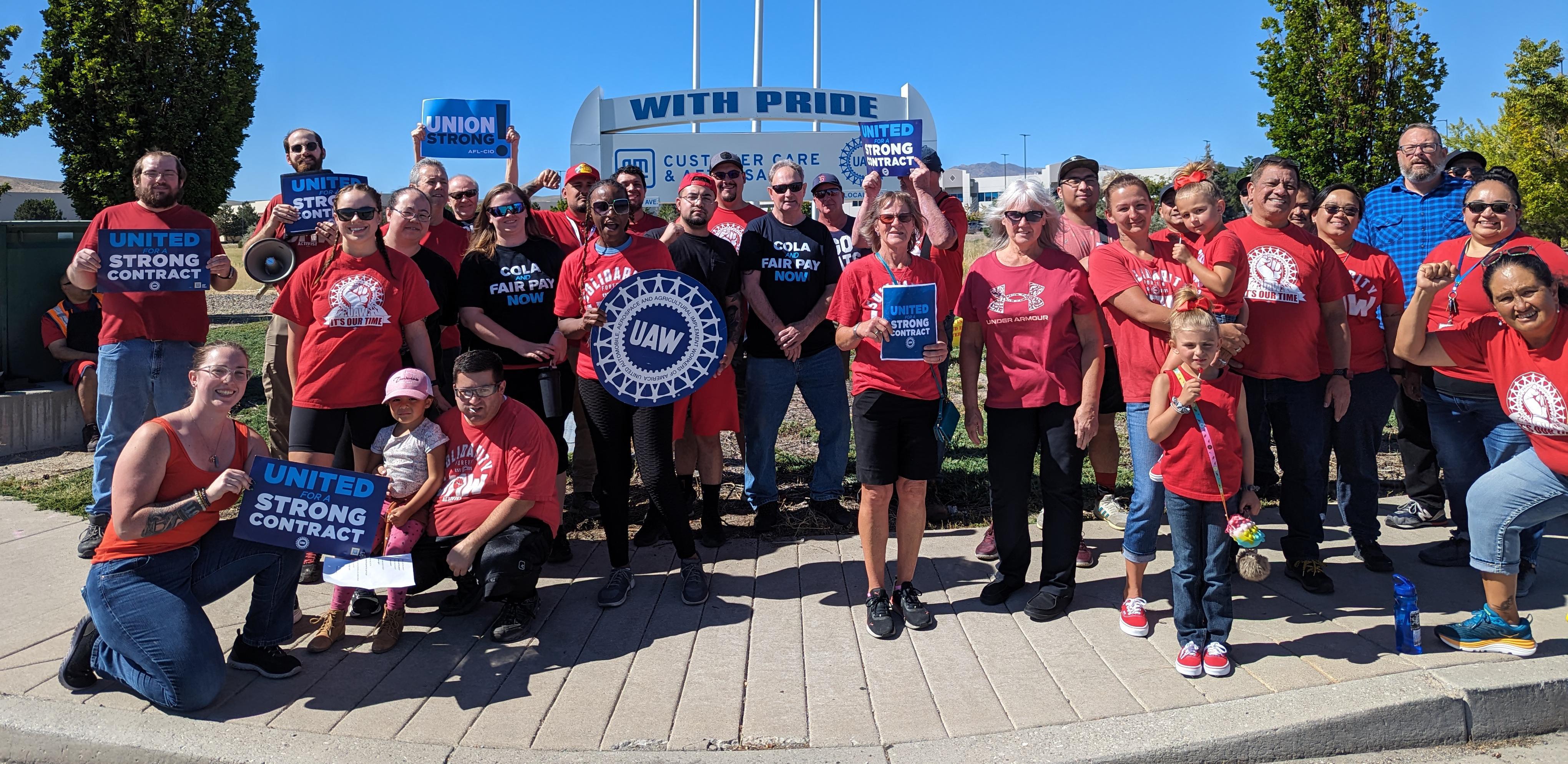 About 30 UAW 2162 members wearing red shirts pose with UAW signs. 