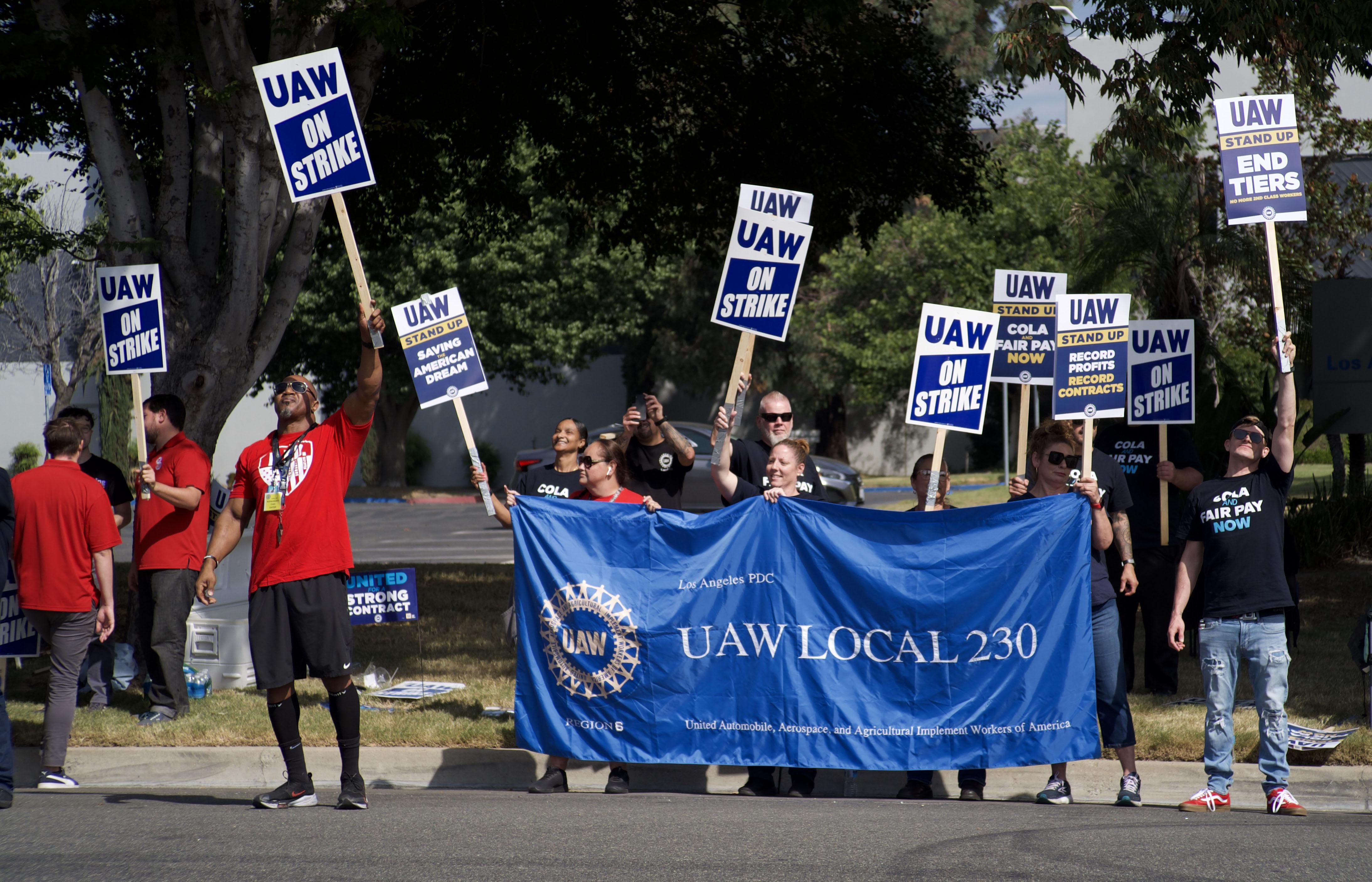 12 UAW 230 members on the picket line, holding a large blue UAW 230 banner 
