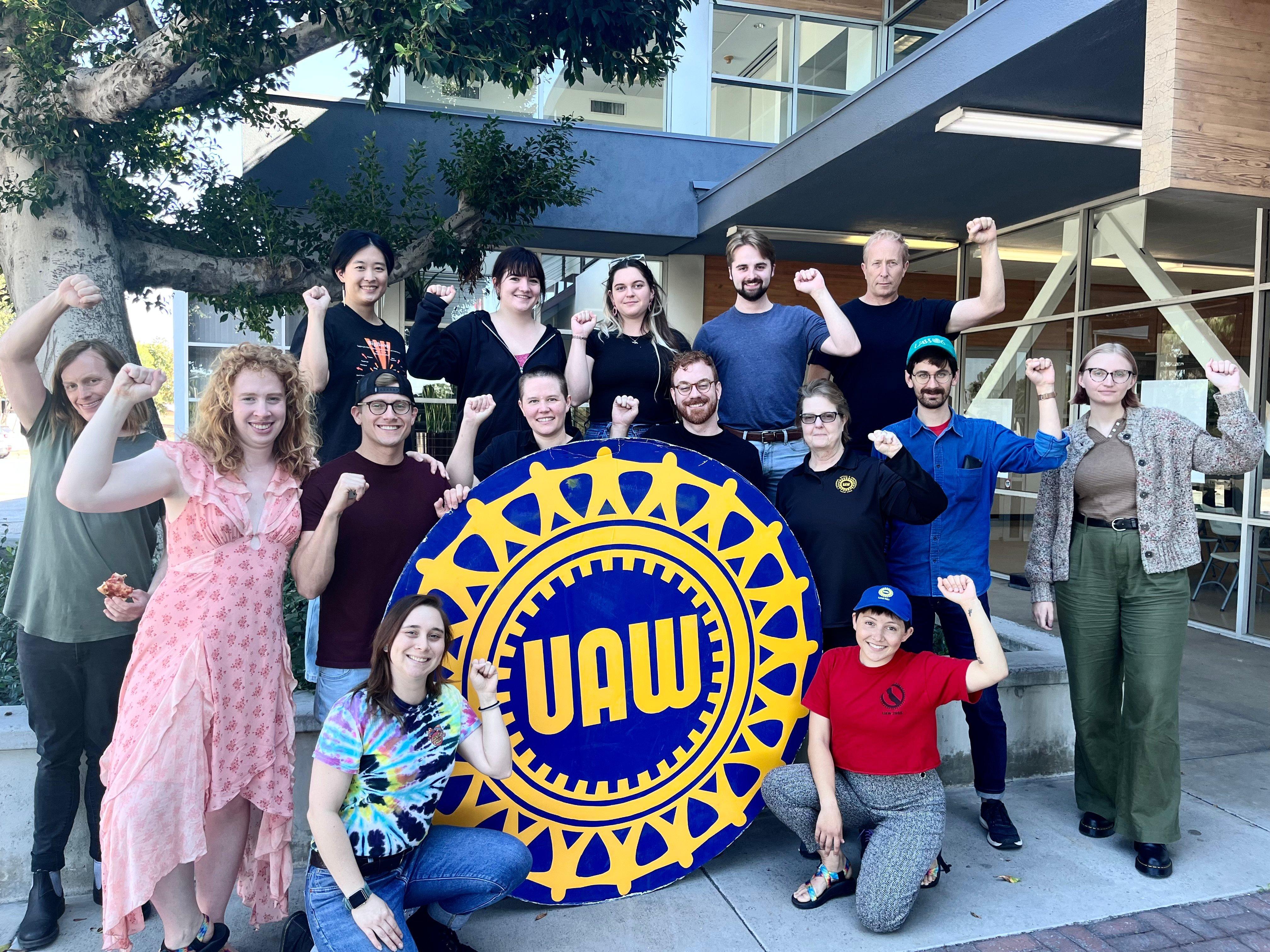 Fifteen UAW members posed for a photo with a large UAW wheel cutout