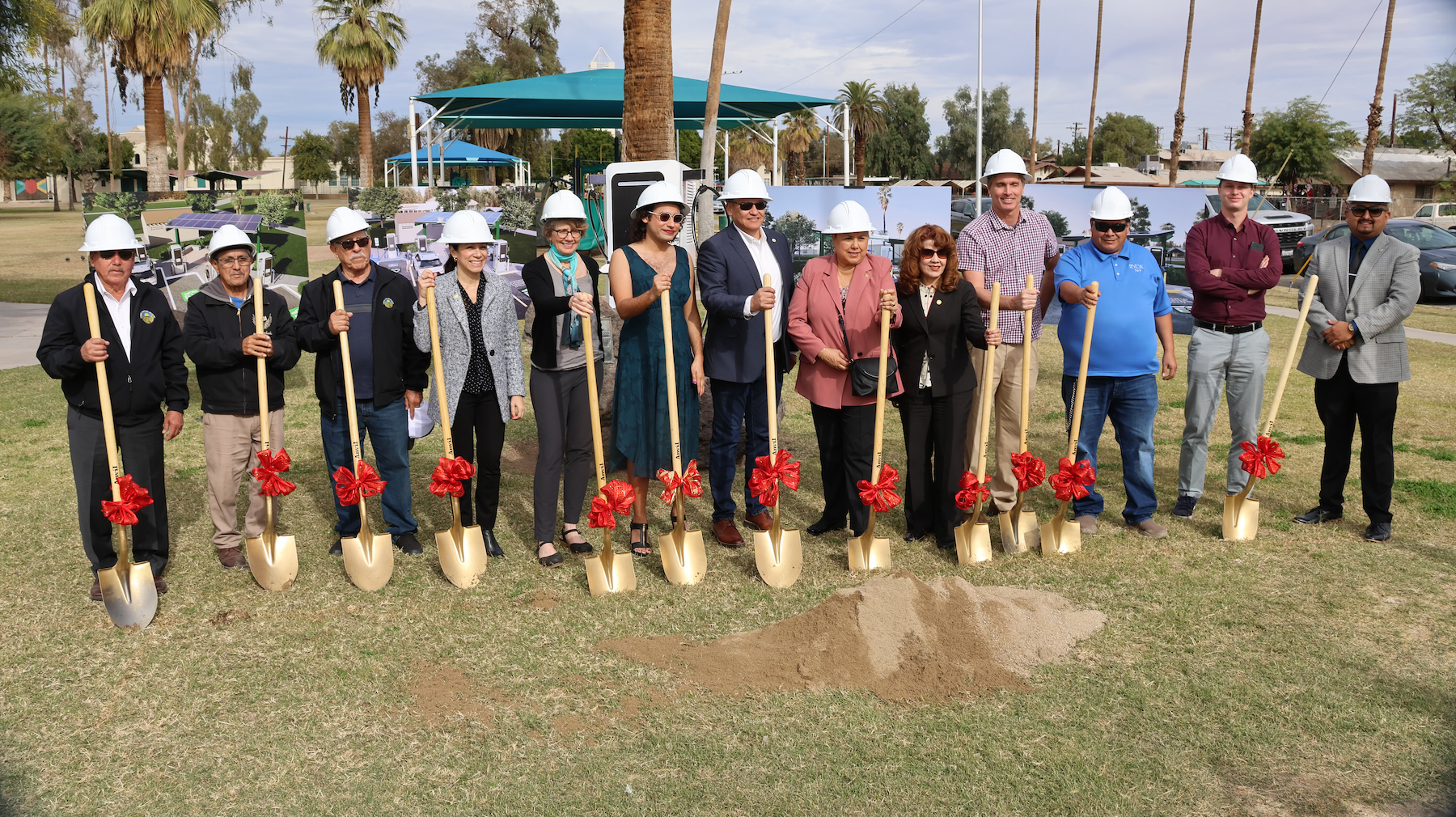 13 people standing in a line holding shovels at a groundbreaking event. 